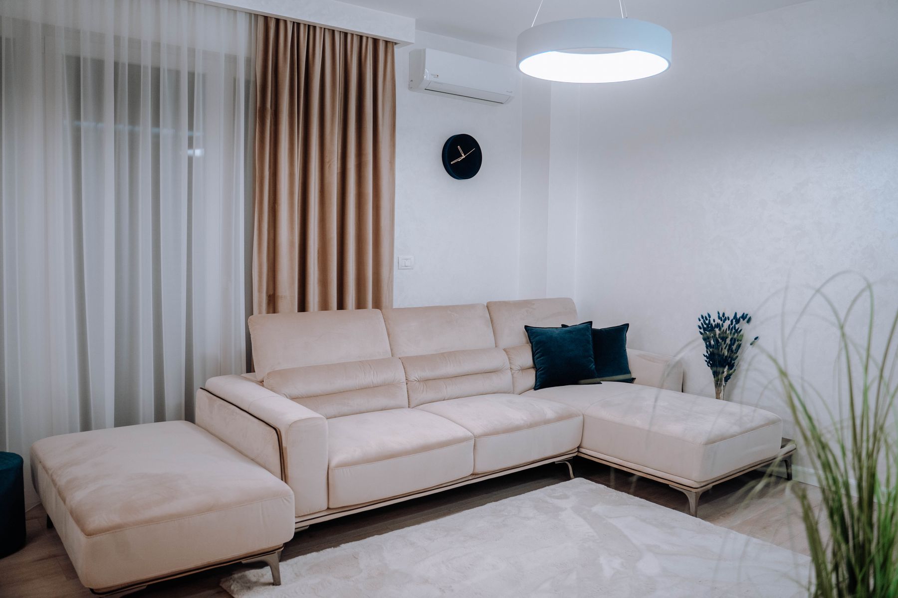 Ruang duduk dengan sofa krem, meja rendah, dan cahaya dari jendela besar